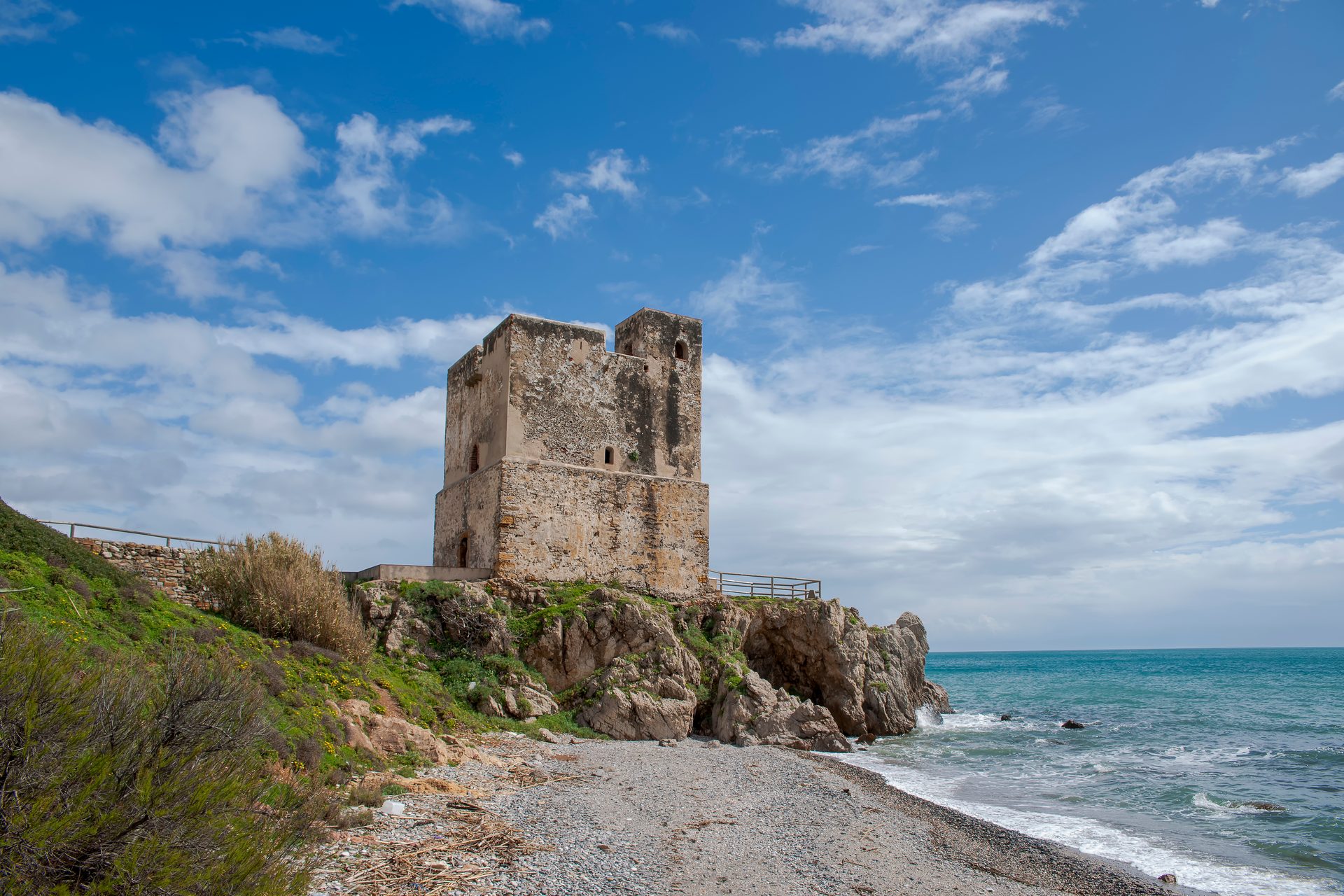 A stone tower on a rocky beach with ocean views and a clear blue sky.